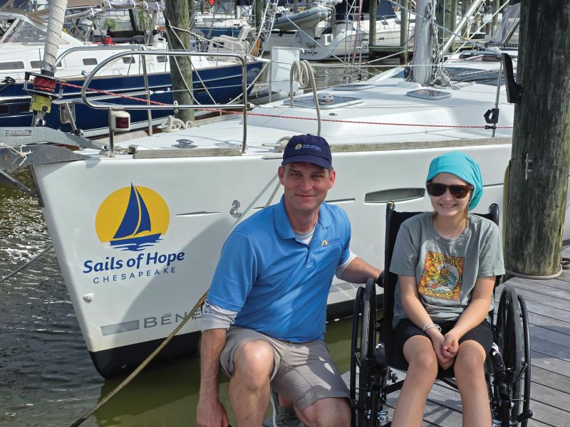 A captain and a guest pose in front of the Sails of Hope Chesapeake's sailing vessel