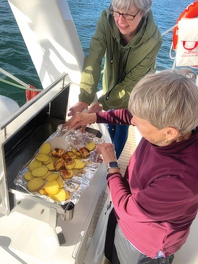 two women grilling food on a sailboat