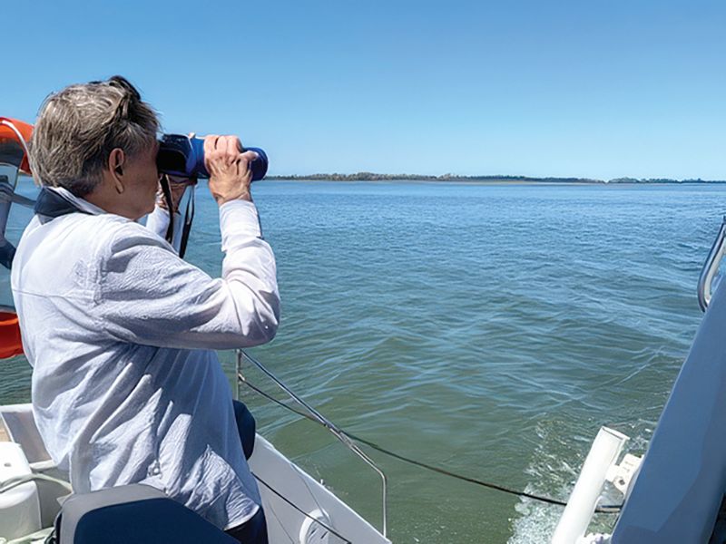 a woman on a boat looking at the shoreline through binoculars