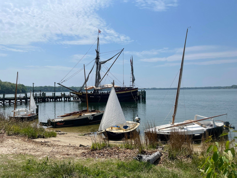 sailboats on a sandy shoreline with a tall ship in the background