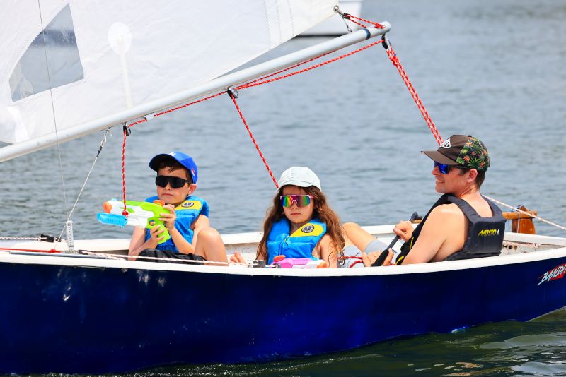 A father and two children sail a Penguin sailboat