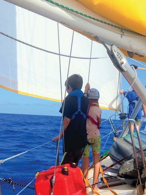 kids on a sailboat watching for dolphins during an ocean passage